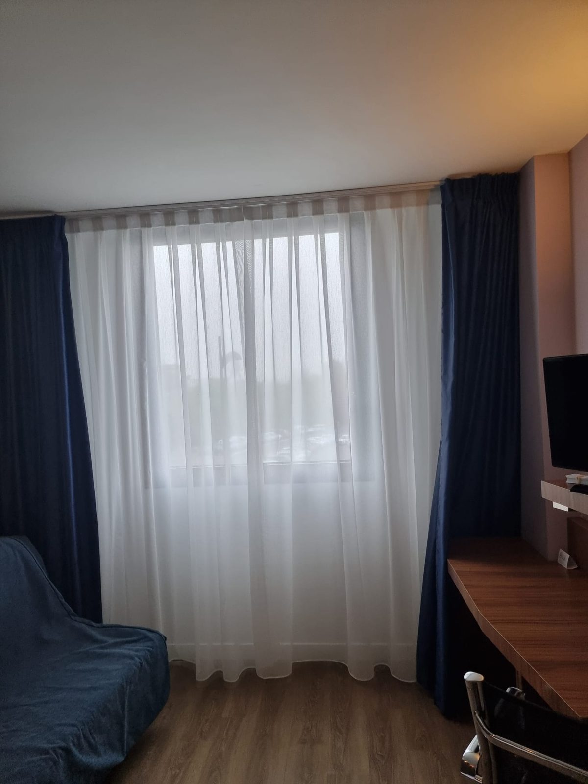 Habitación de hotel con visillo blanco y cortinas azules en la ventana